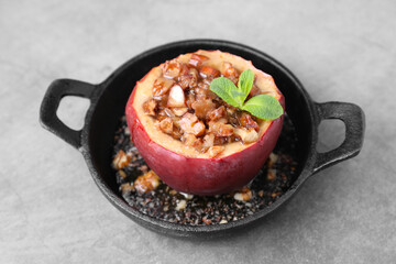 Tasty baked apple with nuts, honey and mint in baking dish on gray table, closeup