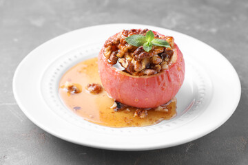 Tasty baked apple with nuts, honey and mint on gray table, closeup