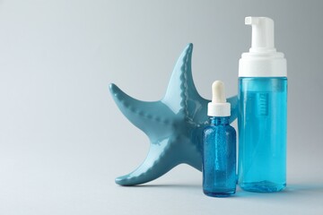 Bottles of cosmetic products and decorative starfish on light grey background, space for text