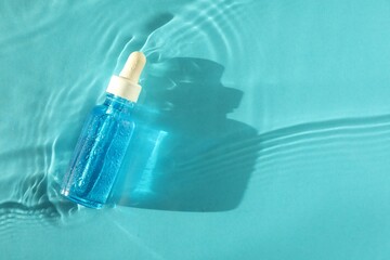 Bottle of cosmetic serum in water on turquoise background, top view. Space for text