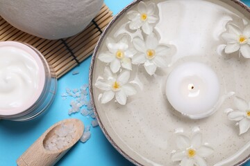 Obraz na płótnie Canvas Beautiful composition with spa products, burning candle and flowers on light blue background, flat lay