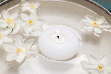 Spa composition with burning candle and beautiful flowers in water, closeup