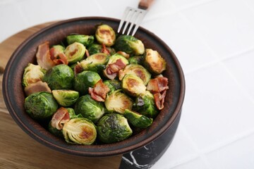 Delicious roasted Brussels sprouts and bacon in bowl on white table, closeup