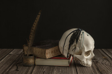 a white skull with teeth next to some old books and a pen to write with ink on a board