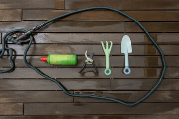 Gardening tools and accessories on a dark plank floor wet from spring rain rolled by a green hose