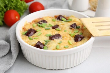 Tasty sausage casserole with green onions in baking dish served on white tiled table, closeup