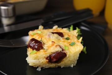 Tasty sausage casserole with green onions and cutlery served on table, closeup