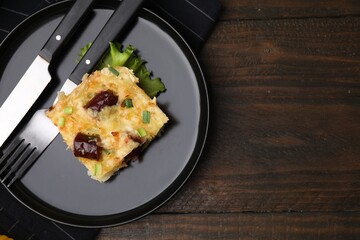 Tasty sausage casserole with green onions and cutlery served on wooden table, top view. Space for text