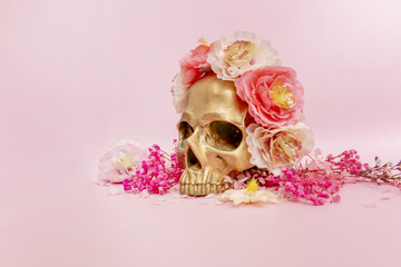 A golden skull adorned with flowers on a soft pink surface posing for photo