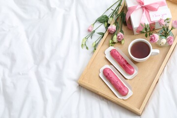 Tasty breakfast served in bed. Delicious eclairs, tea, gift box, flowers and card with phrase I Love You on tray, above view. Space for text
