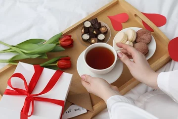  Tasty breakfast served in bed. Woman with tea, desserts, gift box and flowers at home, closeup © New Africa