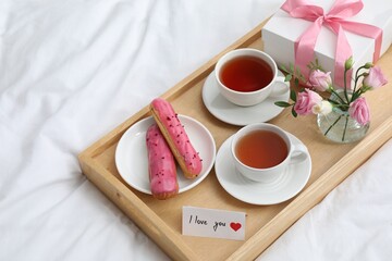 Tasty breakfast served in bed. Delicious eclairs, tea, gift box, flowers and card with phrase I Love You on tray