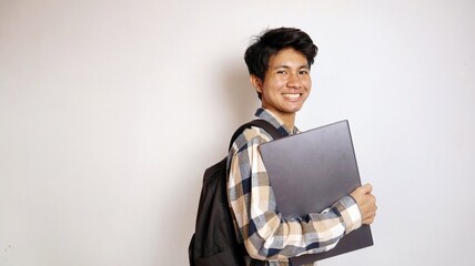 young asian male student wearing earphones and holding laptop