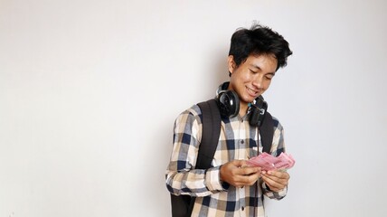 Young Asian man holding a bag is posing counting money