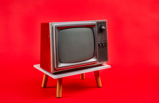 Retro red old television on a stand with blank screen, vintage analog old fashioned TV isolated on red background.