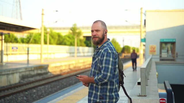 City dweller with a backpack waiting metro train on the platform. An adult heading to work, using a cellphone on public transport. Urban life in the morning as a citizen relies on the subway
