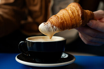 Dipping croissant in a coffee. Delicious morning breakfast with fresh baked croissant and coffee