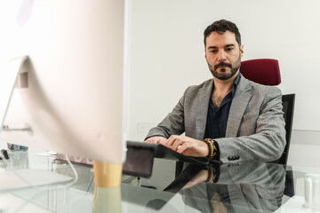 Business executive exudes confidence and focus as he works on his desktop computer in a modern...