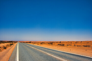 Straight highway through a desolate landscape of dust and red earth in the Western Australian...