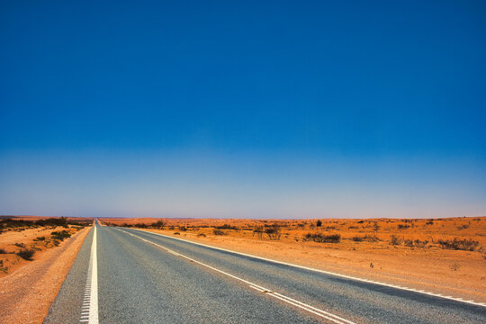 Straight highway through a desolate landscape of dust and red earth in the Western Australian outback, between Exmouth and Coral Bay. 
