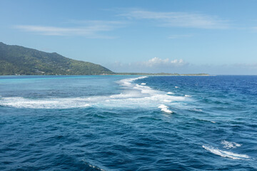Surf breaks over the coral reef separating the shallow turquoise waters of the lagoon surrounding the lush South Pacific island of Mo'orea, French Polynesia, from the blue water of the Pacific Ocean.