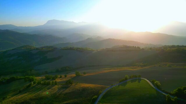 Otherwordly aerial pullback shot from Montefalcone Appennino (Fermo), the sublime and powerful light of the sun piercing through outlined crests and spreading to the surrounding charming Marche hills