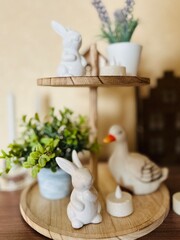Easter spring composition with porcelain rabbit figurines with duck and potted plants on a wooden shelf in the room