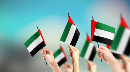 A group of people are holding small flags of United Arab Emirates in their hands.