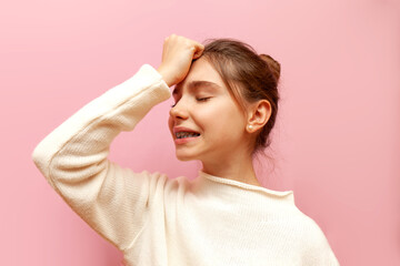 excited teenage girl is worried and shows a facepalm on a pink isolated background, an unhappy...