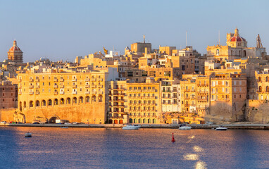 Old stone traditional multi-storey buildings over Valletta Bay on a sunny morning.