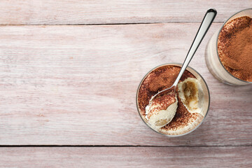 Delicious tiramisu in glasses and spoon on wooden table, top view. Space for text