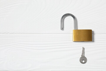 Steel padlock with key on white wooden table, top view. Space for text