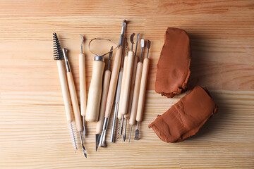 Clay and set of modeling tools on wooden table, flat lay