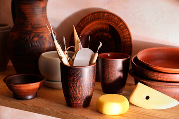 Set of different crafting tools and clay dishes on wooden rack in workshop