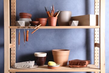 Set of different crafting tools and clay dishes on wooden rack in workshop