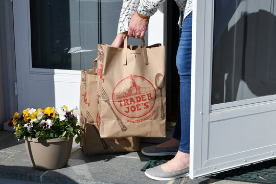 Female picking up Trader Joe's grocery bags from porch that have been delivered