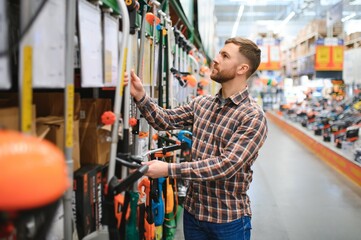 a young man in a gardening equipment store chooses an electric trimmer for mowing lawn grass