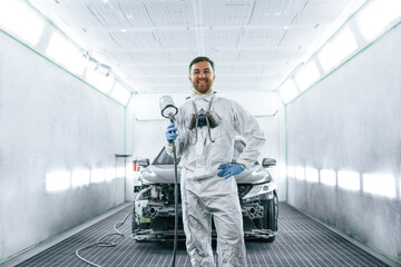 Bright artificial lighting. Man is standing and holding spray gun with paint for automobile