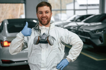 Standing in the garage with cars. Portrait of professional painter with mask