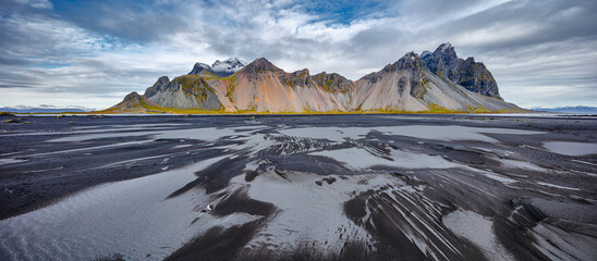 landscape in panorama format of the famous mountain range Vestrahorn with a beach of  wet black and dry grey volcanic sand in the foreground, Iceland
 - Powered by Adobe