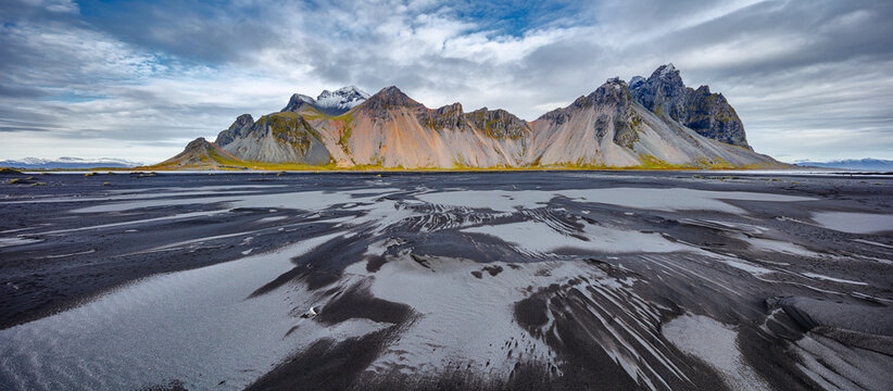 landscape in panorama format of the famous mountain range Vestrahorn with a beach of  wet black and dry grey volcanic sand in the foreground, Iceland

