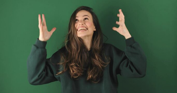 Excited sport fan young woman in green sweatshirt wait for special moment go celebrate win scream rejoices doing winner hands gesture at last isolated on green color wall background.