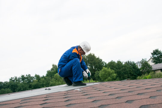 against a background of white sky, and green trees, a man repairs the soft roof of the roof