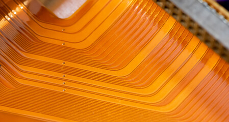 A detailed close-up of a copper colored flexible flat ribbon cable with parallel conductive lines, warm orange abstract technology background texture with copy space, nobody, macro detail closeup