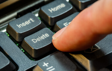 Finger pressing the Delete key on a simple laptop computer keyboard, object macro detail, extreme closeup. Deleting files, removing content, digital data deletion abstract concept symbol, one person