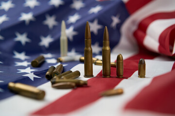 Closeup of cartridges and bullets of different sizes arranged on top of American flag with stars...
