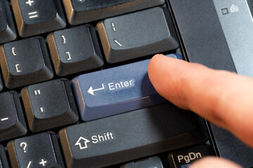Man pressing a blue enter key on a laptop computer keyboard, hand finger object detail closeup,...