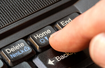 Finger pressing a home button on a simple laptop computer keyboard, object closeup, one person. Home page directory, homepage, going back home real estate abstract concept, home location symbol