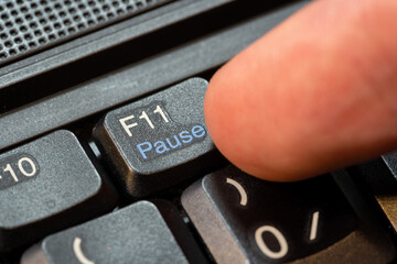 Finger pressing the pause key on a modern laptop computer keyboard, object closeup macro detail, one person.Clicking, pausing an activity, taking a break simple abstract concept, lunch break from work