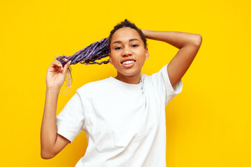 young african american woman with dreadlocks holding her hair in her hands on a yellow isolated...
